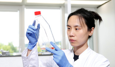 Junge Forscherin betrachtet eine rote Flüssigkeit in einer Glasflasche.